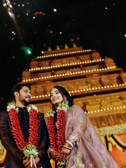 A stunning night shot of the couple after their ceremony, with a grand, illuminated temple-like structure creating a divine backdrop.