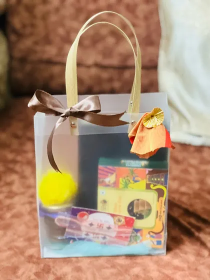 This Rakhi bag is filled with colorful goodies and tied with a simple brown ribbon. The transparent bag offers a sneak peek of the fun items inside.