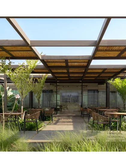 The outdoor cafe at Brigade Oasis is sheltered by a bamboo and steel pergola, creating a beautiful play of light and shadow. This space seamlessly connects the built structure with the lush surrounding landscape and water features.