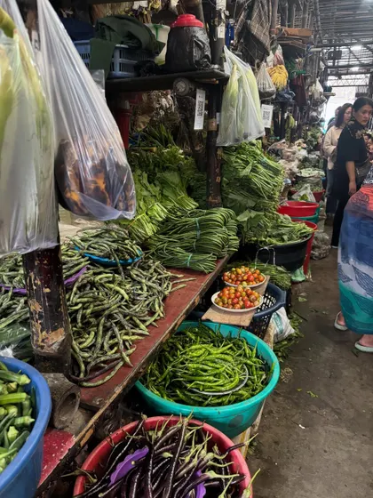 A stall at a Naga market filled with fresh produce like green beans, cherry tomatoes, and bundles of leafy greens. We believe in using the freshest ingredients to create the most flavorful food.