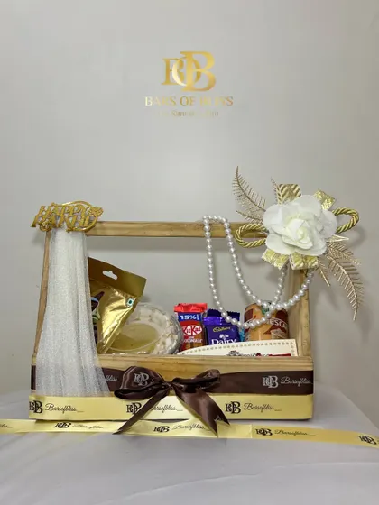 Elegance in a crate. This Raksha Bandhan hamper combines treats and tradition, featuring a caramel swirl cake, assorted chocolates, a coffee can, and a beautiful rakhi, all arranged in a reusable wooden crate decorated with pearls and flowers.