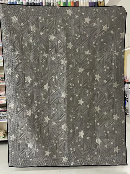 The back of the Twisted Geese quilt, featuring a fun grey fabric with white stars.
