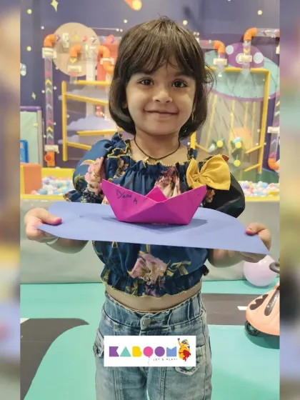A young girl smiles as she displays the paper boat she created. Our simple origami and papercraft activities are perfect for sparking creativity in children.