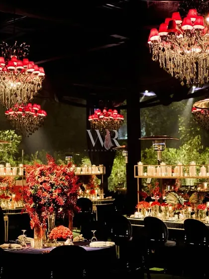This image captures the dramatic effect of the red chandeliers against the dark, draped ceiling. The layers of light and color create a deeply romantic and luxurious dining experience.