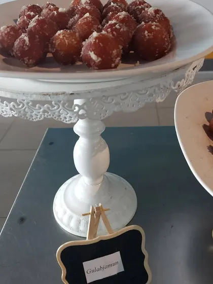 A classic Indian dessert, Gulab Jamun, sprinkled with coconut and served on an elegant white pedestal stand. This was part of a special lunch menu for a corporate event.