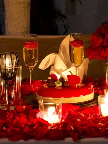 A close-up of a celebration table, featuring a beautiful cake, champagne, and a bed of roses. We can arrange these details for your special occasion.