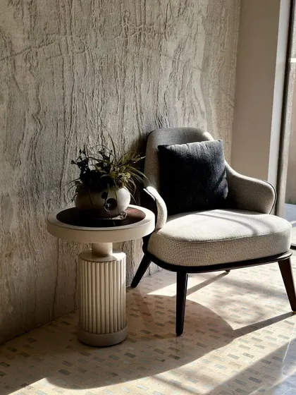 We created this cozy corner as a small sanctuary within a larger space. The structured armchair, with its dark wooden legs and neutral upholstery, is paired with a fluted side table, demonstrating how curated furniture can define an intimate nook.