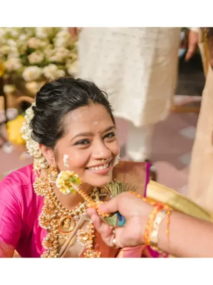 A gentle moment as haldi is applied to the bride's cheek with a flower. Her serene smile and the traditional setting create a beautiful and intimate portrait.