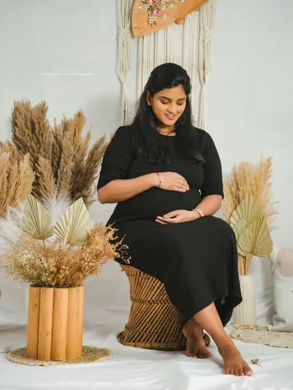 A serene solo portrait of a mother-to-be seated in a boho-chic studio setting, gently cradling her baby bump.