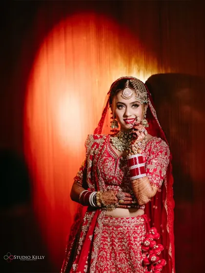 A dramatic bridal portrait with a spotlight effect, highlighting the bride in her stunning red lehenga.