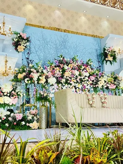 A multi-dimensional stage design featuring pastel blue and white panels, abundant floral arrangements, and elegant chandeliers. This setup creates depth and visual interest for a lavish reception.