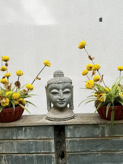A serene corner setup featuring a Buddha head statue flanked by two pots of marigolds, creating a peaceful and contemplative atmosphere.