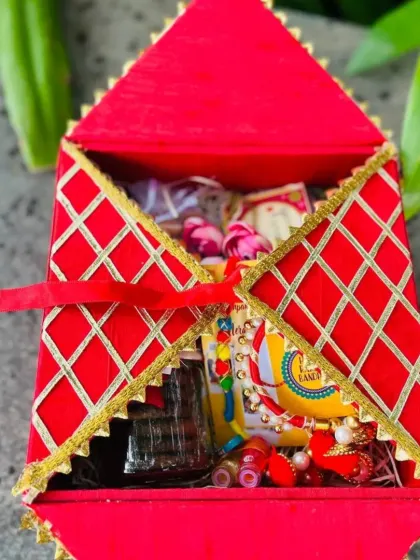 A unique, house-shaped red gift box for Raksha Bandhan, filled with assorted sweets and a rakhi.