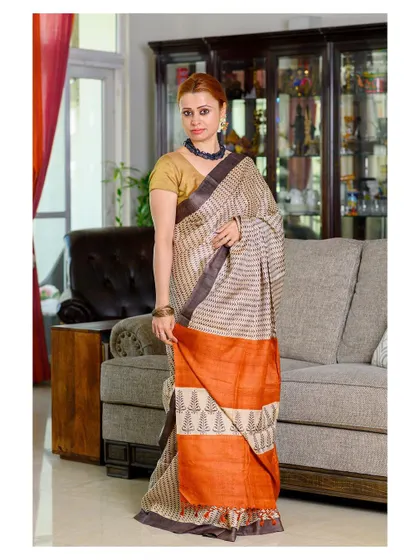 A full-length portrait showcasing a striped tussar silk saree. The indoor home setting gives the image a natural and relatable feel, perfect for a brand that values authenticity.