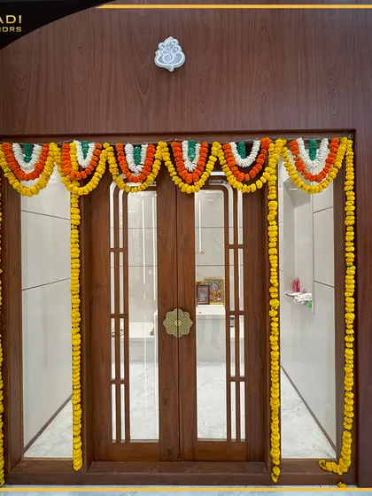 A simple yet elegant wooden puja room door with glass panels, decorated with a colorful marigold garland for a festive occasion.