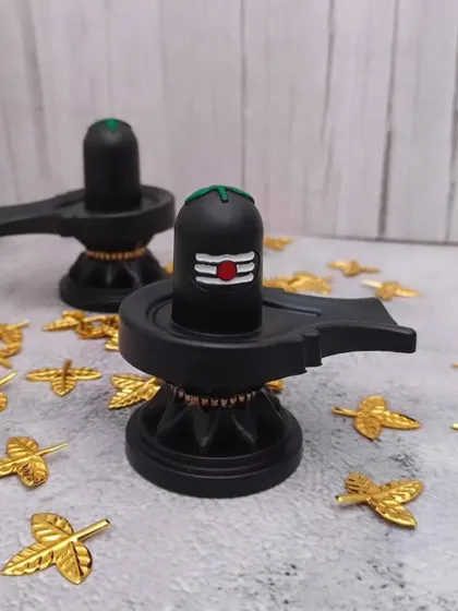 A pair of black Shiv Lingam idols, perfect for observing rituals like Maha Shivaratri. The golden leaves are for archana.