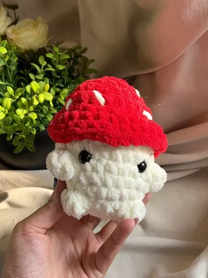 A tiny, adorable mushroom toy made with chunky yarn. The red cap with white spots is a classic, cute design that makes a perfect small gift or decoration.