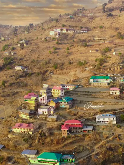 A wide drone shot showing the village of Dharech spread across the hillside. This captures the scale and beauty of life in the mountains.