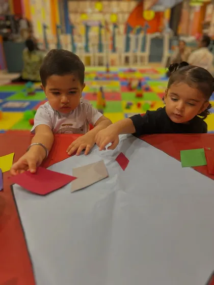 Toddlers at a shared table work on their individual kite crafts, developing focus amidst the group setting.