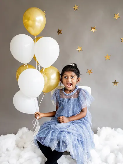 Among the stars for a stylish fifth birthday studio session. The simple grey backdrop with gold stars and balloons allows this little girl's sparkling personality and beautiful blue dress to shine.