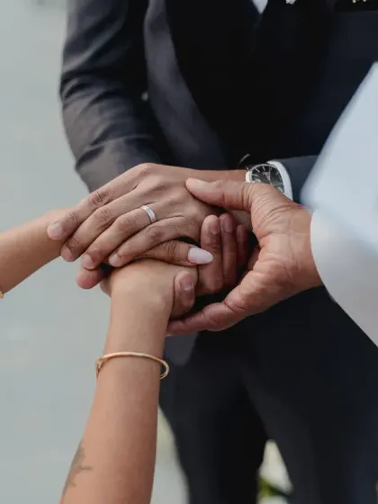 A close-up of hands during the vow exchange, showing the wedding bands and the joining of two lives.