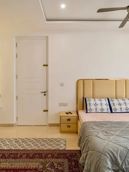 A serene bedroom designed with minimalism and luxury in mind, featuring an upholstered headboard, soft lighting around the vanity mirror, and textured rugs for warmth.