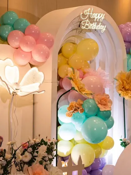 This floral garden theme uses a rainbow of pastel balloons flowing through an arched white backdrop. The lit floral elements add a magical glow, perfect for an enchanting birthday celebration.