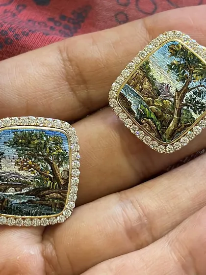 A close up of my "Chapter of Forest" earrings held in my hand. Each earring is a miniature landscape painting, a wearable piece of art that tells a story of nature and tranquility.