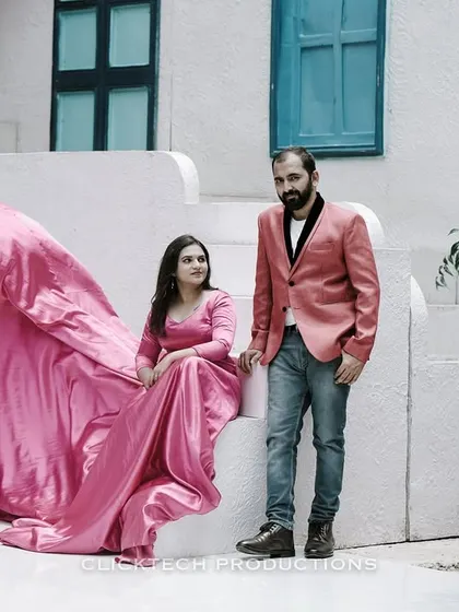 A couple poses on a set of white stairs, the bride's pink trail gown spread out, creating a romantic and visually appealing pre-wedding photograph.