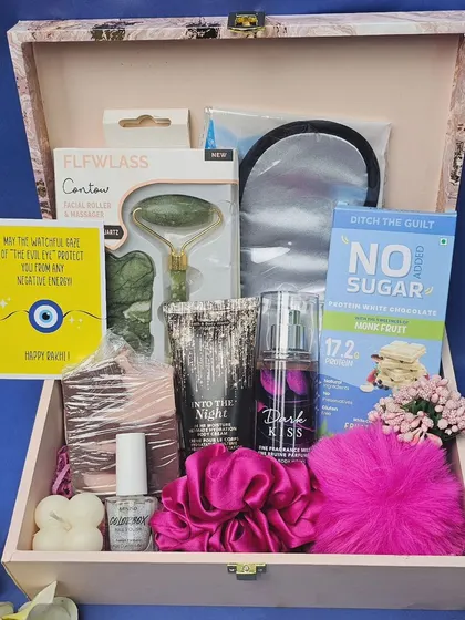 A luxurious Rakhi hamper designed for a sister. This wooden trunk box is filled with a jade roller, an eye mask, perfume, nail polish, a scrunchie, a protein bar, and other pampering goodies.