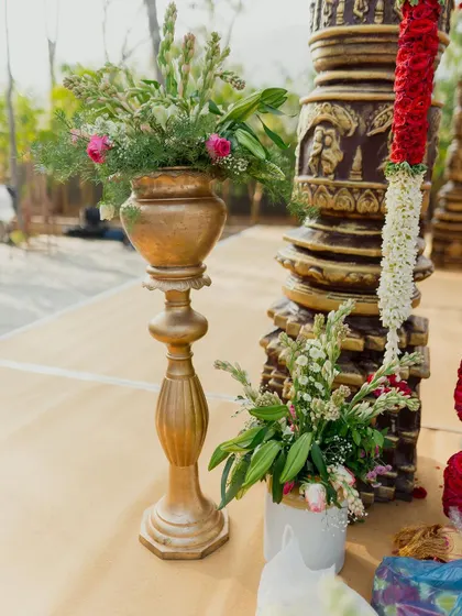 A detail shot from a South Indian wedding, showing a tall brass floral stand next to a traditionally carved pillar and a vibrant flower garland. These elements are key to creating an authentic atmosphere.
