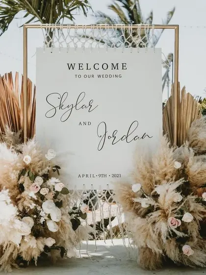 A stylish boho-themed welcome sign, decorated with pampas grass and dried palm leaves for a modern, rustic feel.