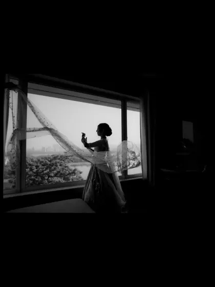 A dramatic silhouette of the bride against a large window, her veil catching the light.