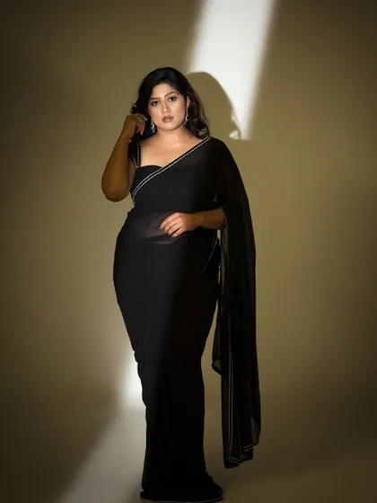 A full-length shot of the model in a sheer black saree, looking elegant and mysterious.
