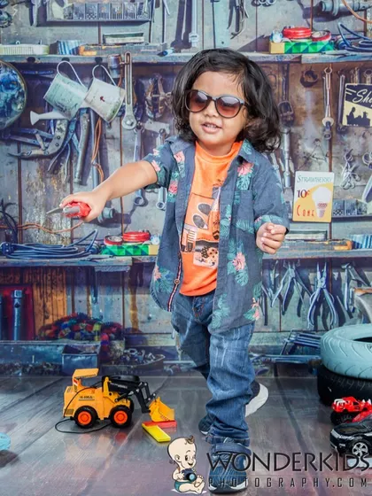 A cool little mechanic at work in our garage-themed studio. With his sunglasses and screwdriver, he looks ready to fix the toy excavator in this detailed and playful setup.
