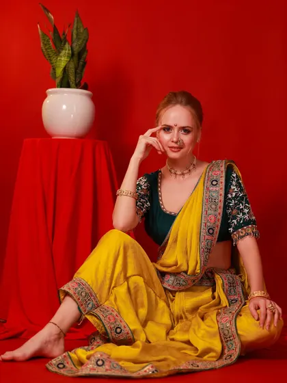A full-length seated portrait from the festive series. The composition includes a simple prop, adding context and balance to the vibrant colors of the saree.