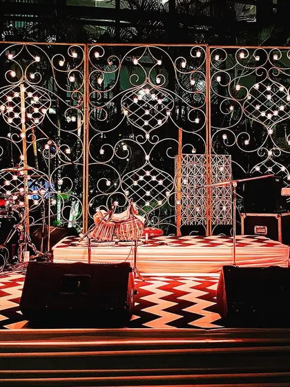 A unique stage backdrop created from wrought iron panels with integrated lights, designed for a Diwali celebration. This setup includes a drum kit, indicating readiness for a live music performance.
