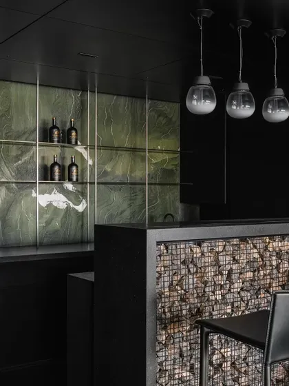 This bar, part of a larger architectural gesture, features a Gabion wall facia. We contained randomly sized stones within a metal wire mesh to introduce a raw, textural element that contrasts with the monolithic black surfaces, creating a point of material drama and interest.
