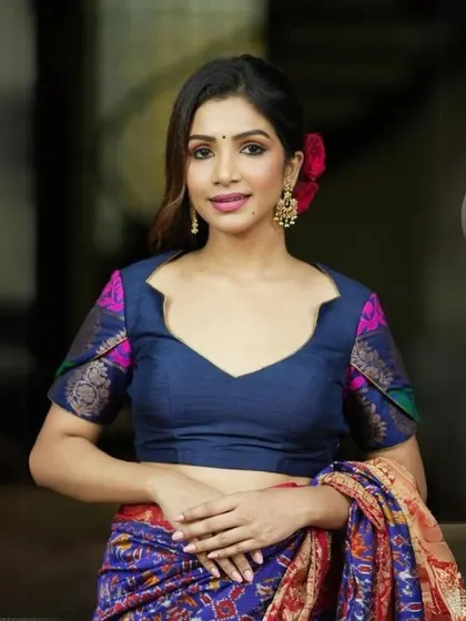 A model wears a navy blue blouse with contrasting printed sleeves, paired with traditional gold earrings.