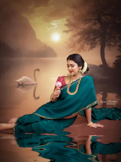 A fine art composition with a painterly feel. The mother-to-be, in her green saree, interacts with a flower by a dreamy, swan-filled lake at sunset.