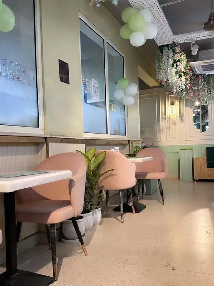 The interior of this charming cafe uses a soft color scheme of pastel pink and mint green. The design includes comfortable upholstered chairs, marble-topped tables, and decorative wall paneling for an elegant feel.