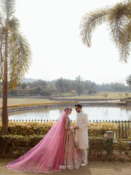 A stunning wide-angle shot of the couple by a lake, the bride's long pink veil creating a dramatic and romantic effect.