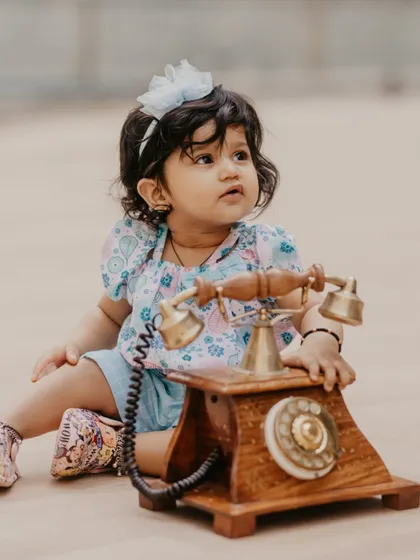 A thoughtful moment during a poolside first birthday shoot, featuring a baby girl and a classic rotary telephone.