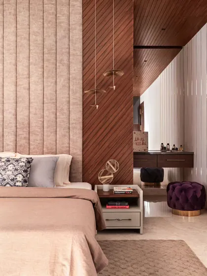 This bedroom plays with different textures and materials. The soft, upholstered headboard contrasts with the diagonal wood paneling and the sleek vanity area in the background. The pendant lights add a touch of glamour.