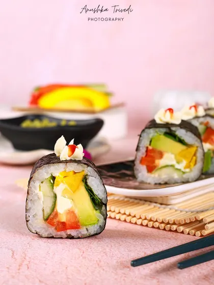 A close-up of a single piece of vegetable sushi, highlighting the fresh avocado, cucumber, and bell pepper inside.