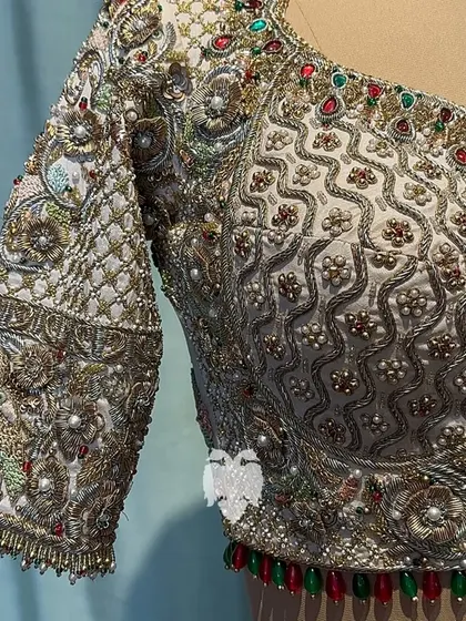 A close-up of the intricate embroidery on the Radha Krishna blouse, showing the vibrant 3D parrots and floral bed.