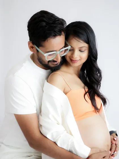 A modern and chic couple's portrait. The mom-to-be shows off her bump in a stylish crop top and open shirt, held lovingly by her partner.