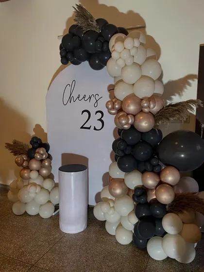 An elegant and modern "Cheers to 23" birthday setup. This features a minimalist white backdrop with a chic balloon arrangement in black, white, and rose gold.