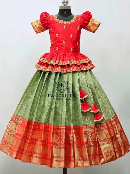 A red and olive green lehenga with a tiered peplum top. The red blouse has simple gold butti work, and the green skirt has a traditional red and gold Kanchi border.