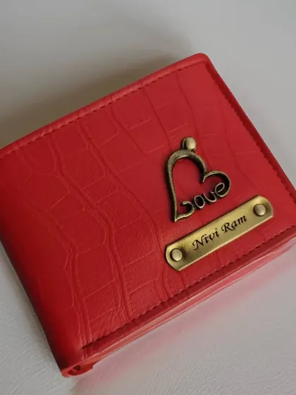 A vibrant red crocodile-textured wallet featuring a "love" charm. The bright color and personal touch make this a standout accessory.